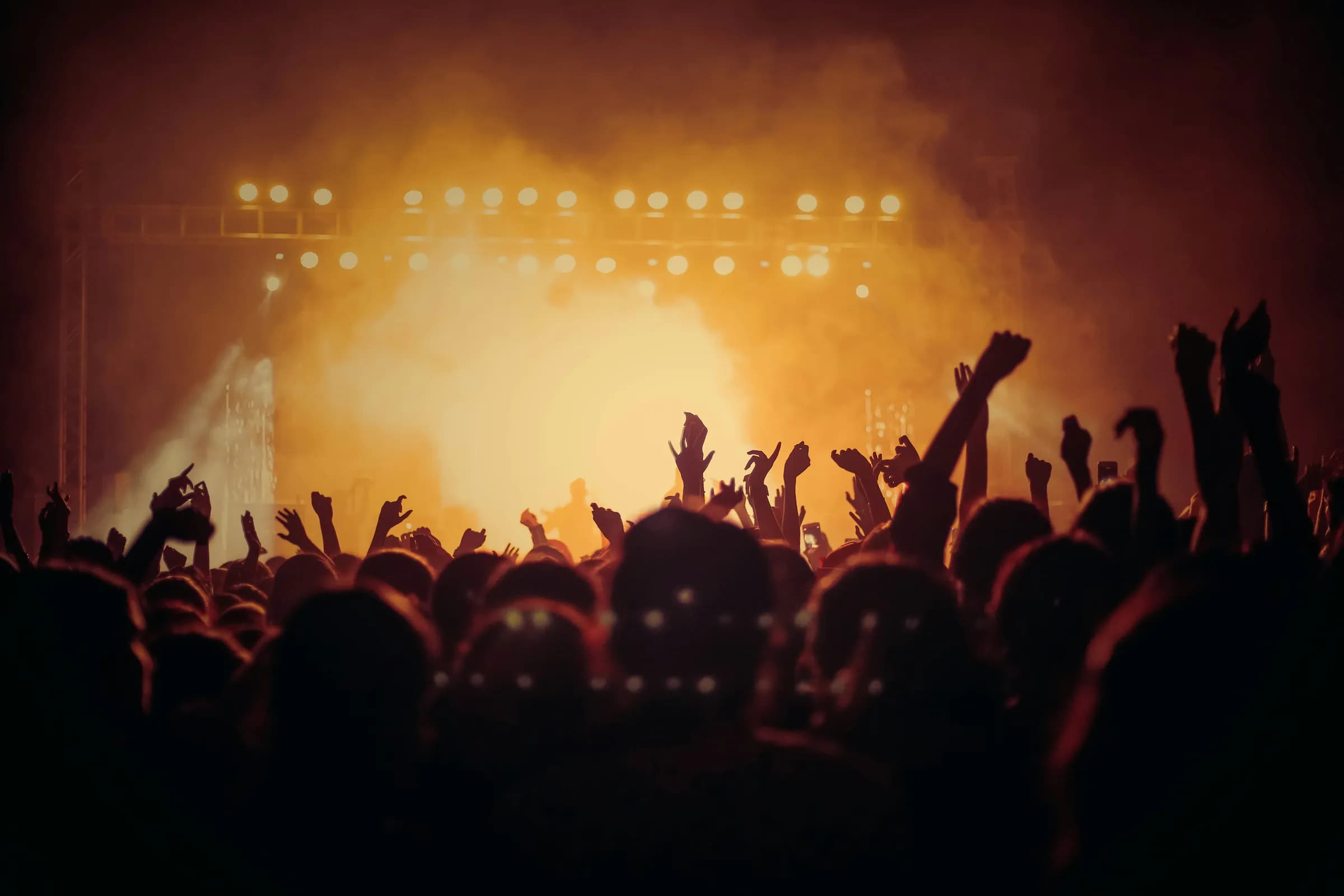 Raised hands in silhouette against an amber-lit stage.
